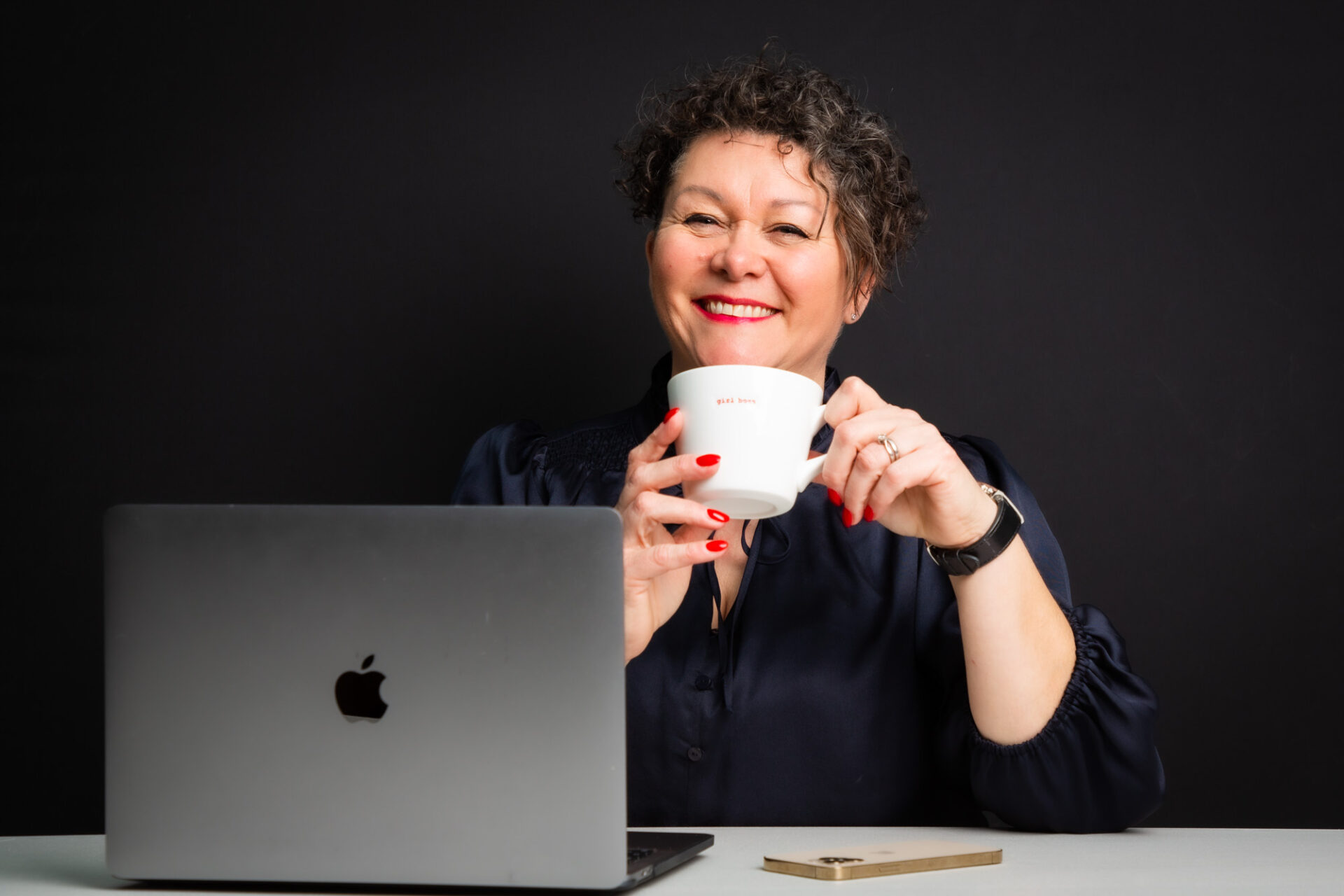 Sue Davies holding coffee cup at desk with laptop