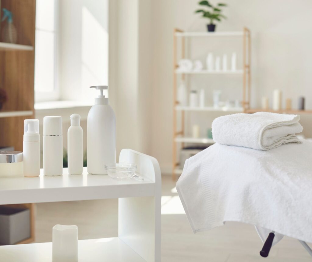 Salon set up showing white product bottles, massage bed with white towels and shelving in the background with product bottles on