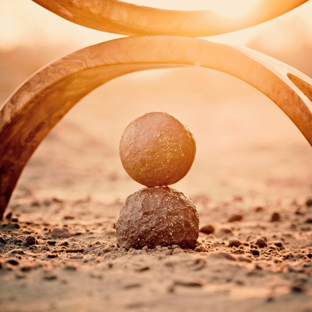 Two round stones balancing one on top of the other with arched structures balancing above in sunrise
